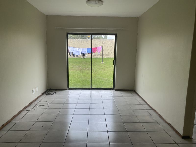 An empty living room featuring tiled flooring and a large sliding glass door providing direct access to the rear garden area.