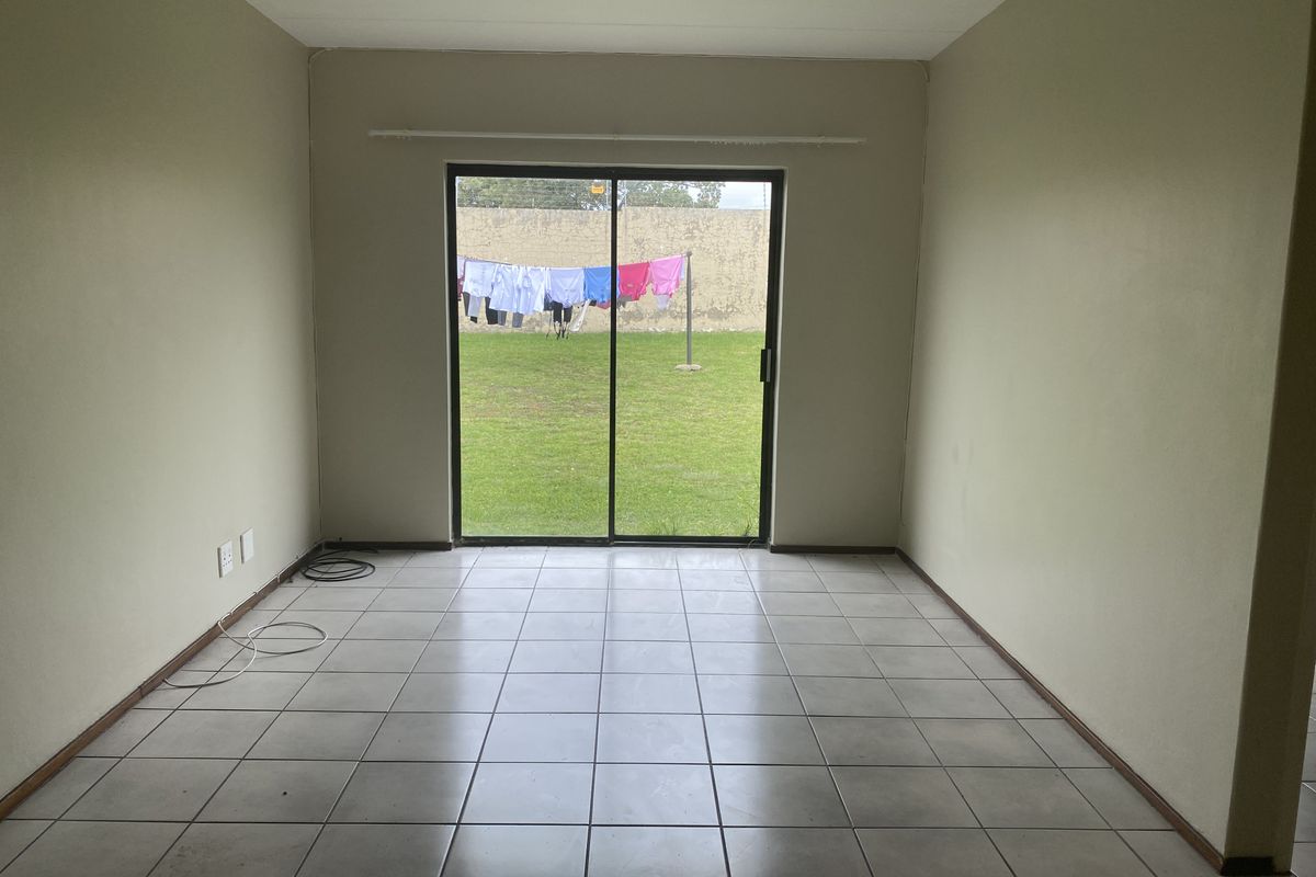 An empty living room featuring tiled flooring and a large sliding glass door providing direct access to the rear garden area.
