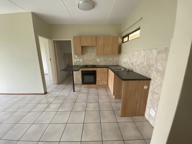 A functional kitchen featuring light wood-finish cabinetry, dark laminate countertops, a built-in oven with hob, and neutral tiled flooring and backsplash.