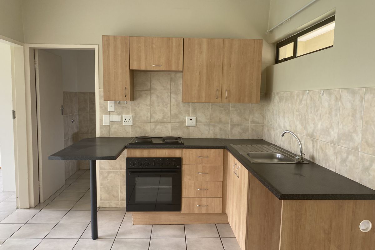 A functional kitchen featuring light wood-look cabinetry, a built-in oven with electric hob, dark countertops, and tiled flooring.