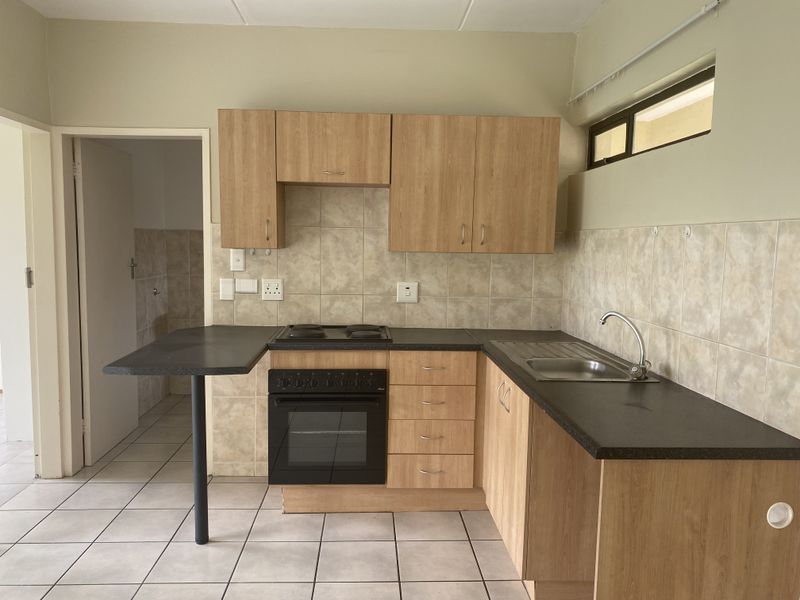 A functional kitchen featuring light wood-look cabinetry, a built-in oven with electric hob, dark countertops, and tiled flooring.