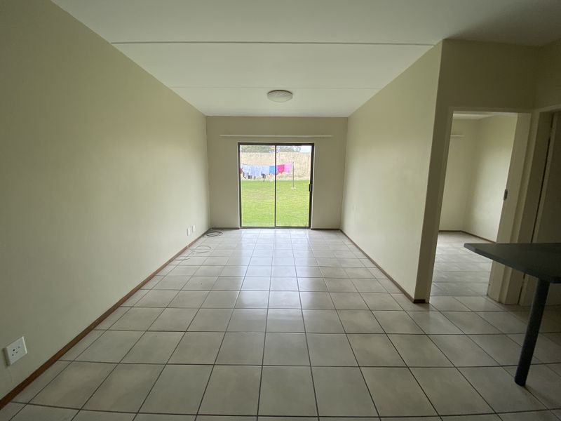 An empty open-plan living area featuring neutral walls, tiled flooring, and a sliding glass door providing access to the rear garden.
