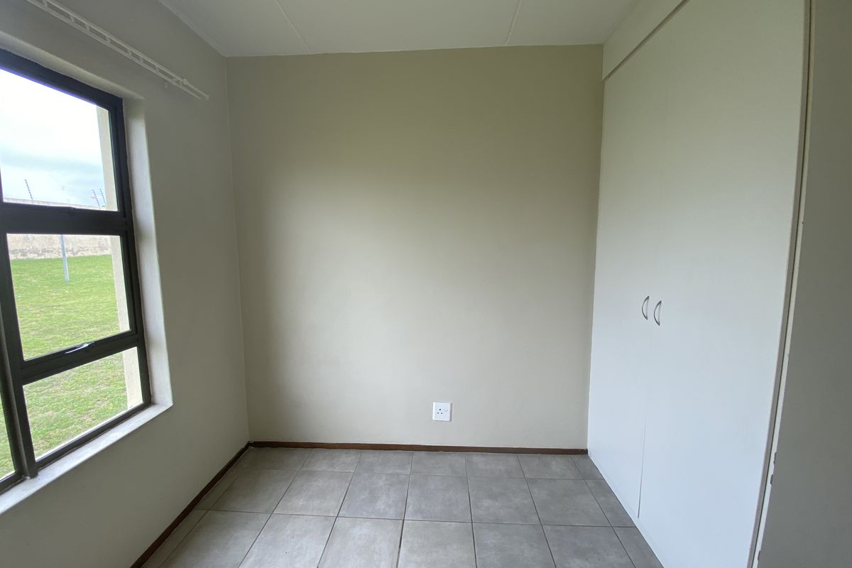 A clean, empty bedroom featuring neutral walls, tiled flooring, and built-in cupboards, offering a versatile space ready for personalization.