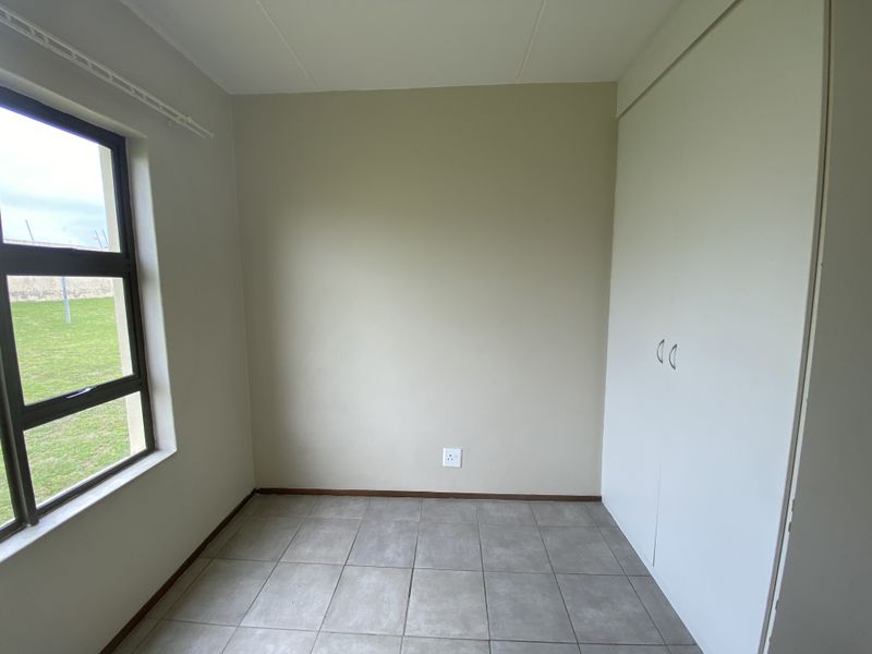 A clean, empty bedroom featuring neutral walls, tiled flooring, and built-in cupboards, offering a versatile space ready for personalization.