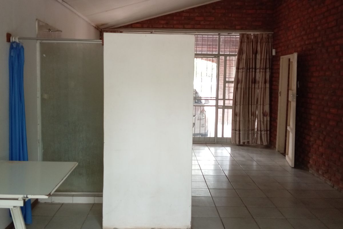 An interior space featuring exposed brick walls, tiled flooring, and a partitioned shower area with direct access to an exterior entrance.