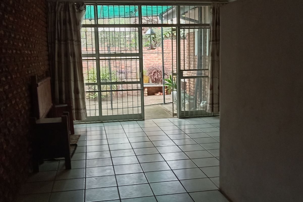 An interior living space featuring tiled flooring, exposed brick wall, and large metal-framed glass doors leading to an outdoor patio area.
