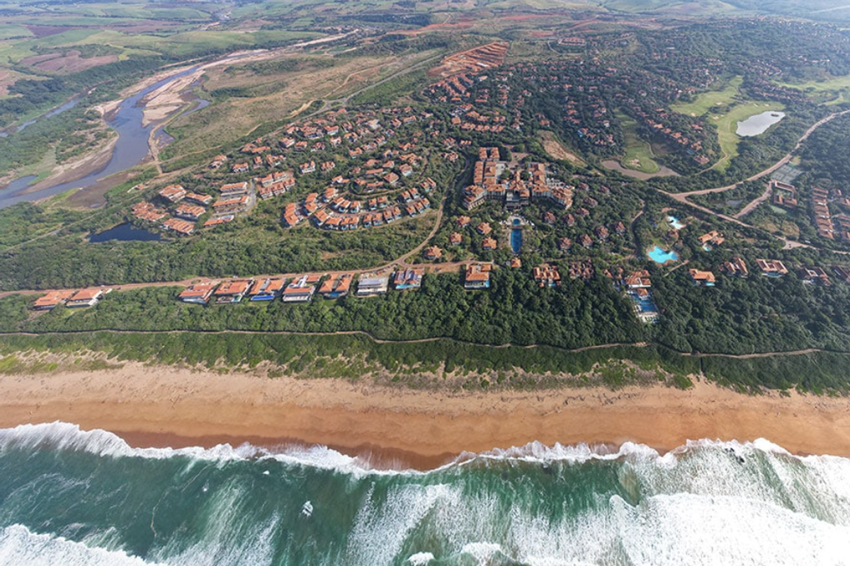 An expansive aerial view of a coastal residential estate featuring lush greenery, proximity to the beach, and integrated community amenities.