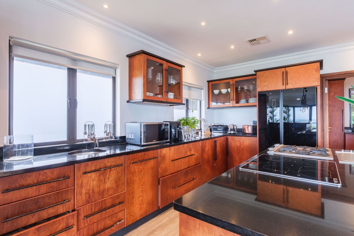 A well-appointed kitchen featuring rich wood cabinetry, sleek black granite countertops, a built-in gas cooktop, and recessed ceiling lighting.