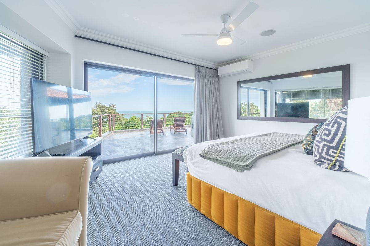 Spacious bedroom featuring a ceiling fan, wall-mounted air conditioning unit, and large sliding glass doors opening onto a private balcony with scenic views.