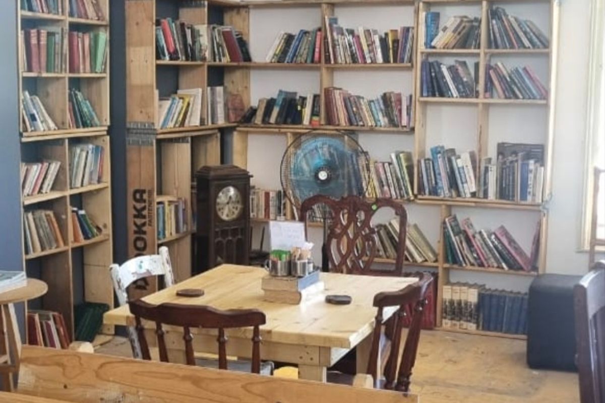 A cozy living area featuring extensive built-in wooden shelving units, pendant lighting, and a neutral color palette, suitable for a library or reading space.
