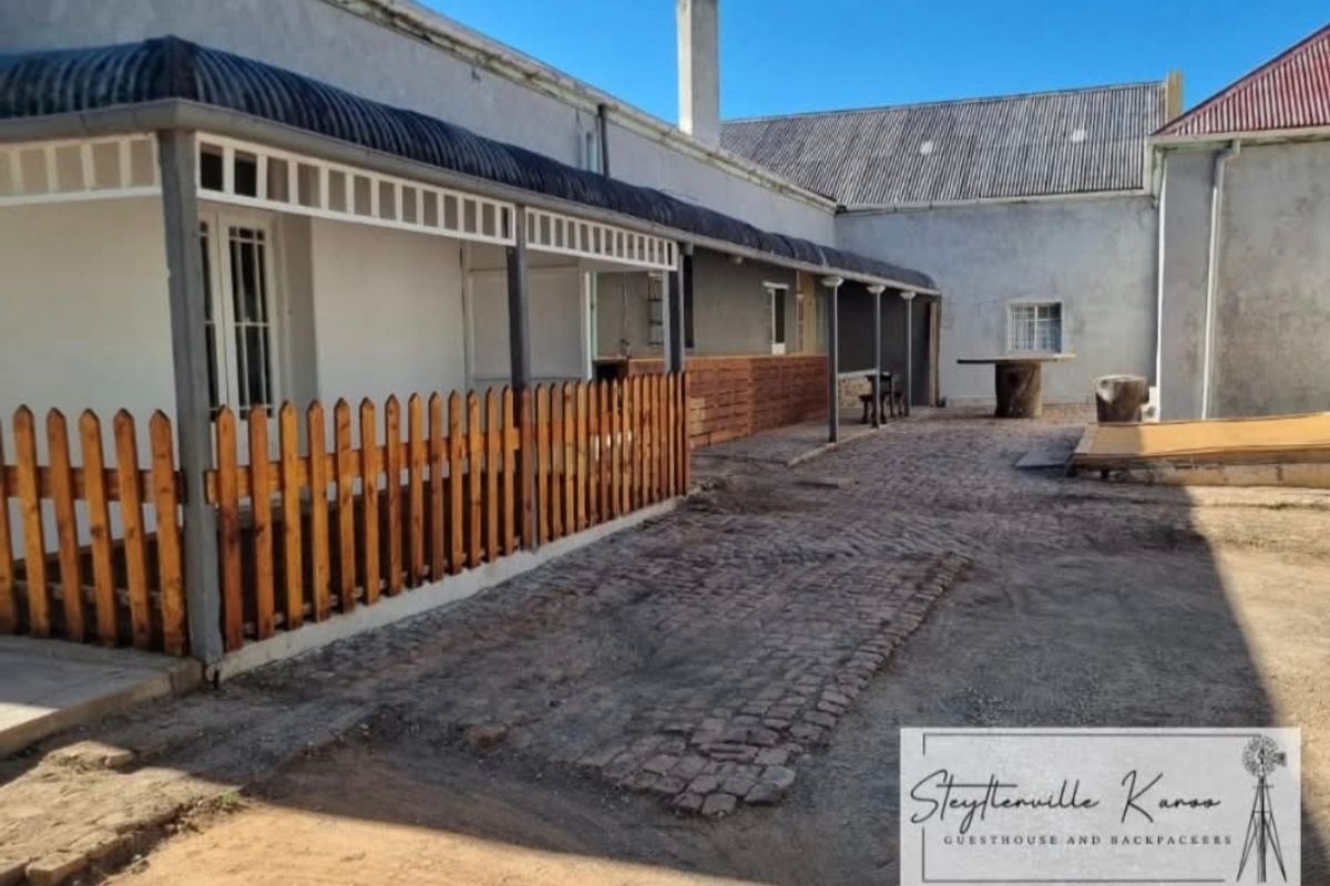A rear exterior view of the property featuring a covered veranda, timber fencing, and a rustic paved courtyard area.