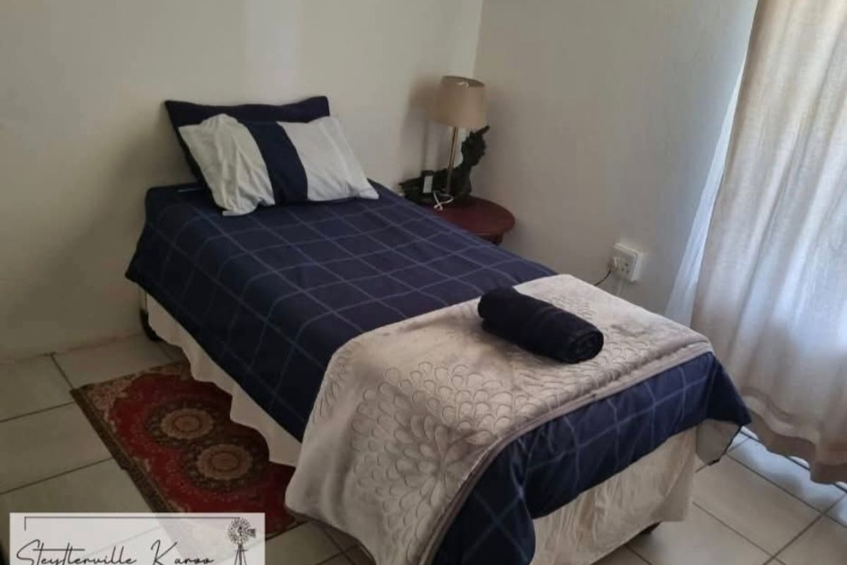 A simple bedroom featuring tiled flooring and a window with curtains, providing a functional and modest sleeping space.