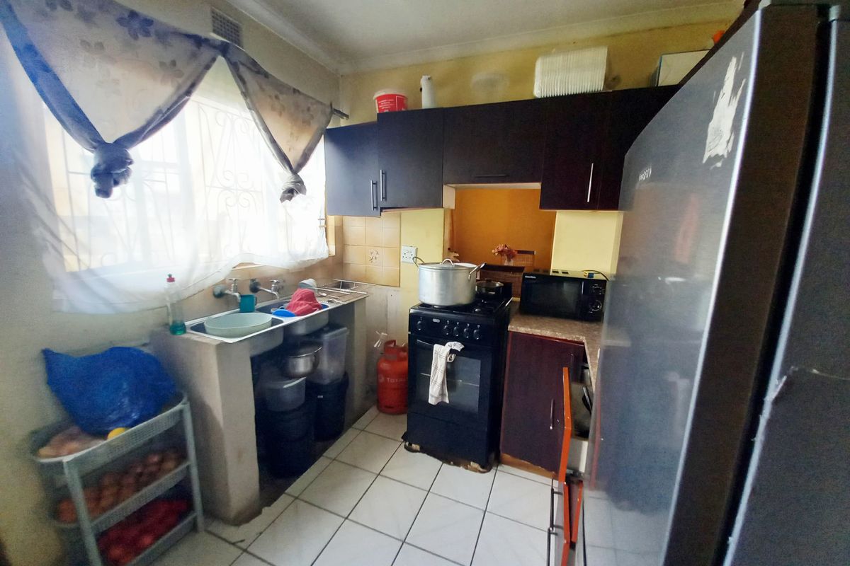 A compact kitchen featuring dark cabinetry, a freestanding stove, double basin sink, and tiled flooring, requiring some cosmetic updates to modernize the space.