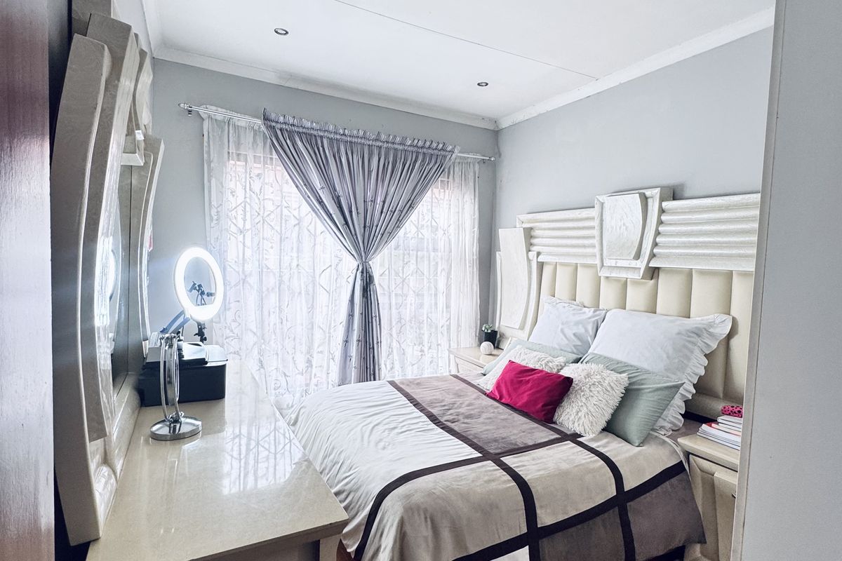 A well-maintained bedroom featuring laminate wood flooring, a built-in headboard, and large windows with curtains, offering a comfortable and functional living space.