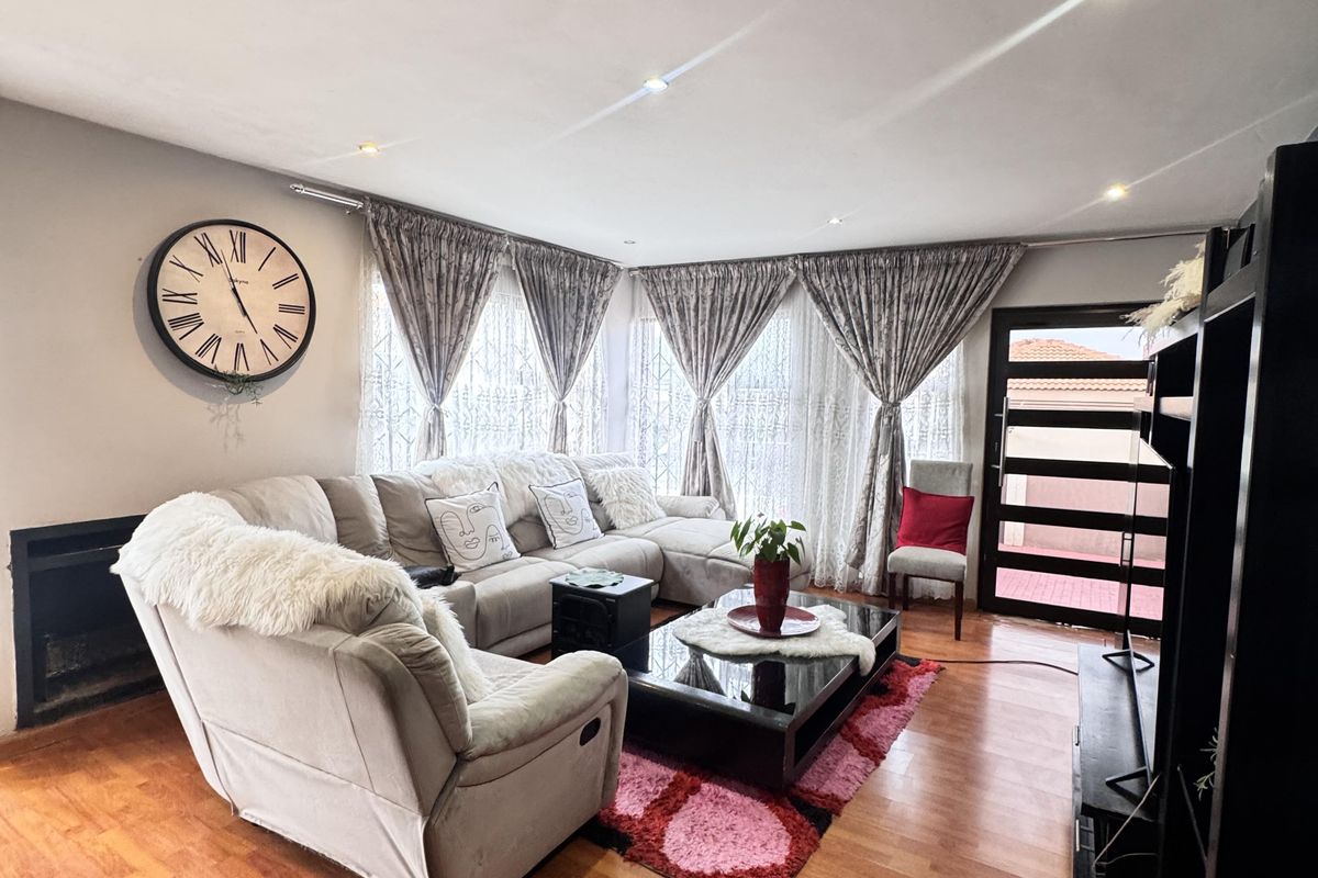 A well-maintained living room featuring warm wood-look flooring, recessed ceiling lighting, and a built-in fireplace, creating a comfortable and inviting atmosphere.