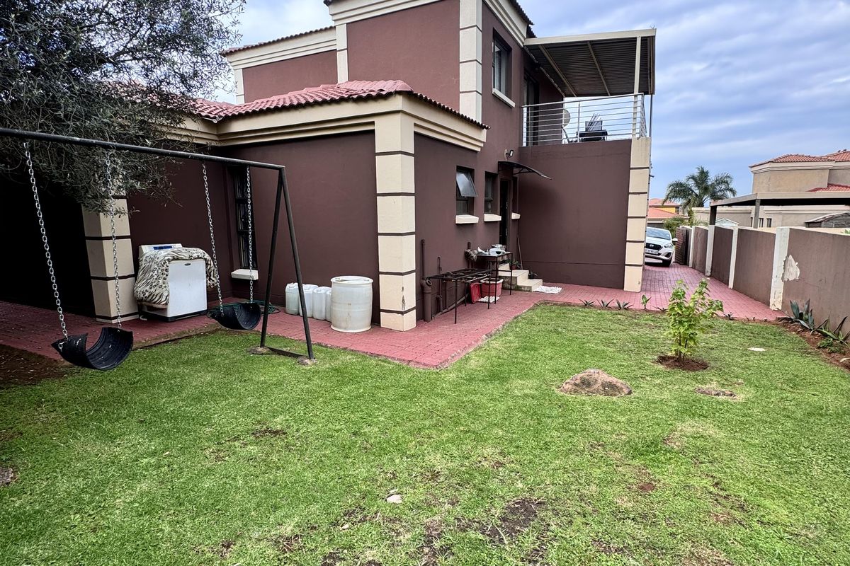 Rear view of the double-story house featuring a paved patio area, a private garden, and an upper-level balcony with metal railings.