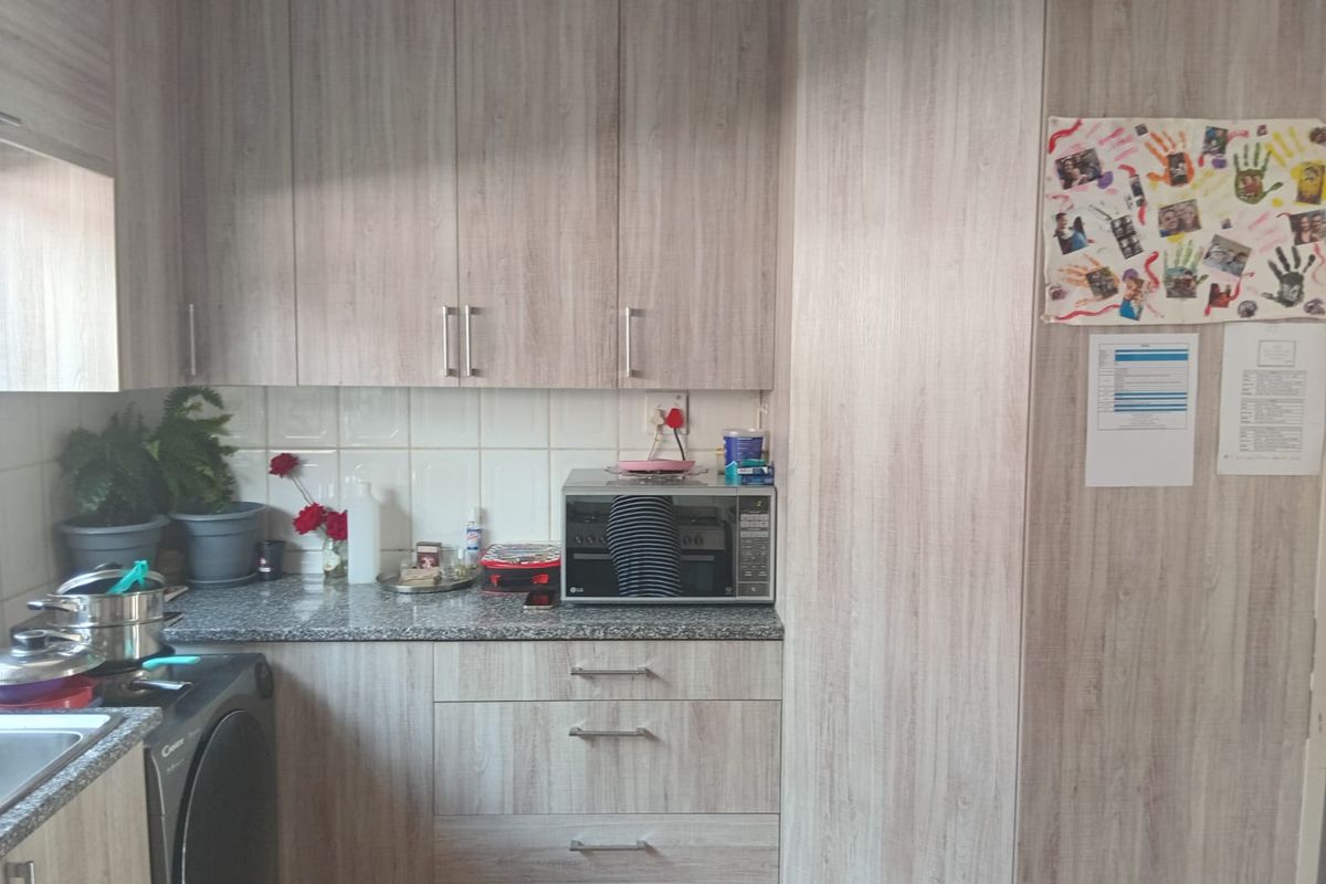 A functional kitchen featuring light wood-grain laminate cabinetry, granite countertops, and a tiled backsplash with integrated microwave and sink area.