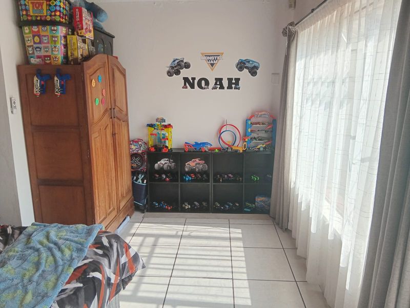 A bedroom featuring tiled flooring and large windows with curtains, providing natural light and a functional layout for a child's room.