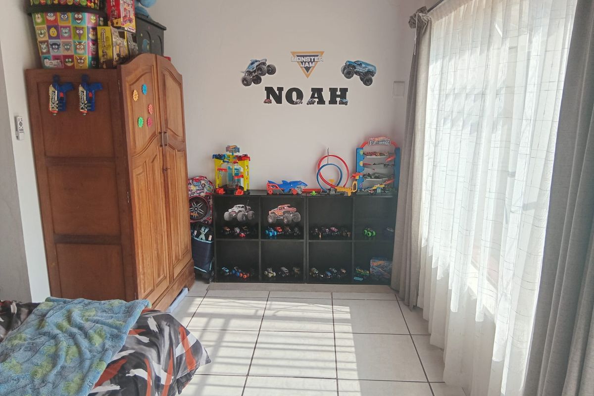 A bedroom featuring tiled flooring and large windows with curtains, providing natural light and a functional layout for a child's room.
