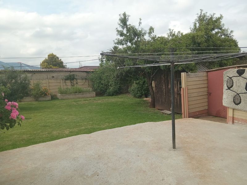 A private rear garden featuring a concrete patio, established lawn, raised garden beds, and a storage shed enclosed by a precast boundary wall.