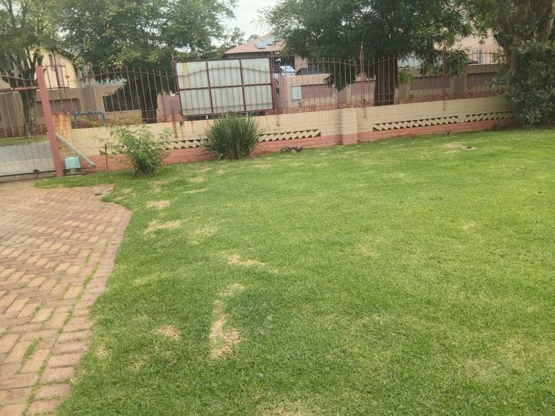 A private garden area featuring a lawn, brick paved pathway, and secure perimeter wall with wrought iron fencing.