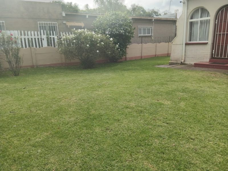 A well-maintained lawn area featuring a perimeter precast concrete wall with security spikes and window security bars on the adjacent building structure.