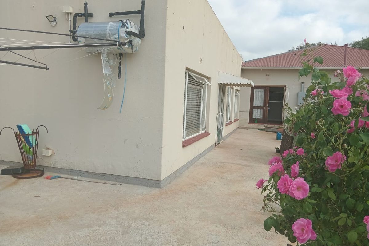 Rear exterior view of the cottage featuring a concrete patio area, external geyser unit, and security bars on the windows.