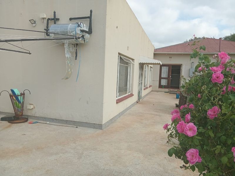 Rear exterior view of the cottage featuring a concrete patio area, external geyser unit, and security bars on the windows.