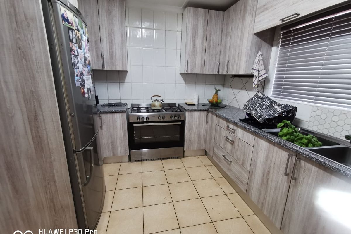A functional kitchen featuring light wood-grain laminate cabinetry, granite countertops, a stainless steel gas oven, and tiled flooring with a neutral backsplash.