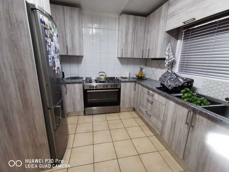 A functional kitchen featuring light wood-grain laminate cabinetry, granite countertops, a stainless steel gas oven, and tiled flooring with a neutral backsplash.