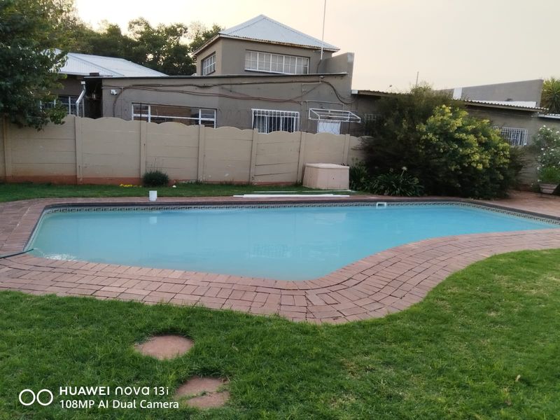 A backyard pool area featuring a swimming pool with brick coping, surrounded by a lawn and a precast concrete boundary wall.