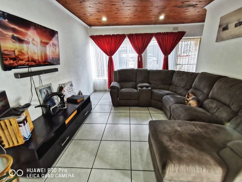 A living room featuring tiled flooring, a timber-paneled ceiling with recessed lighting, and security features on the windows and doors.