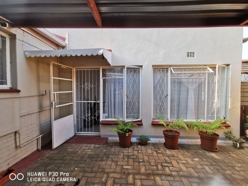 Rear exterior view of the cottage featuring a paved patio area, security gates, and metal window frames under a covered roof section.