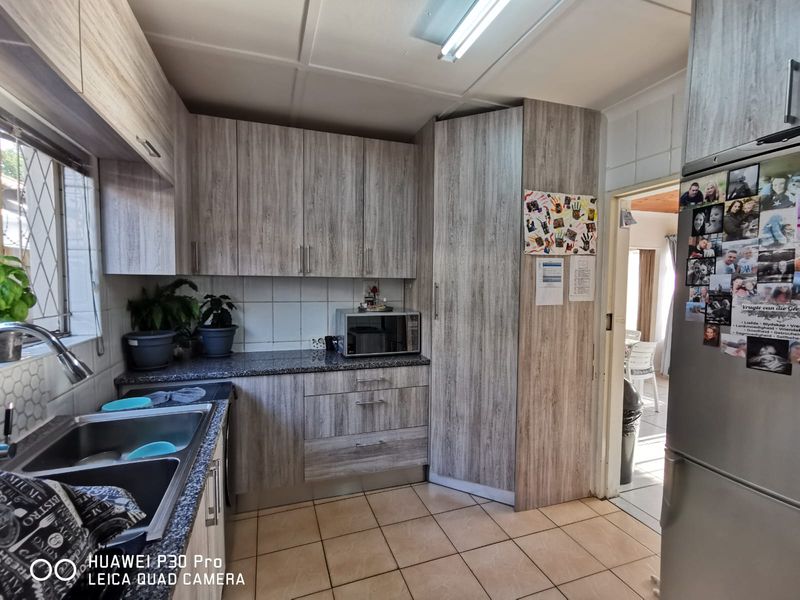 A functional kitchen featuring wood-look laminate cabinetry, granite countertops, a double stainless steel sink, and tiled flooring with a tiled backsplash.