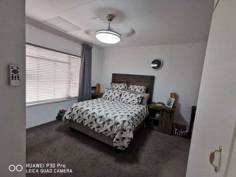 A bedroom featuring carpet flooring, a ceiling fan, and venetian blinds, providing a functional and comfortable sleeping space.