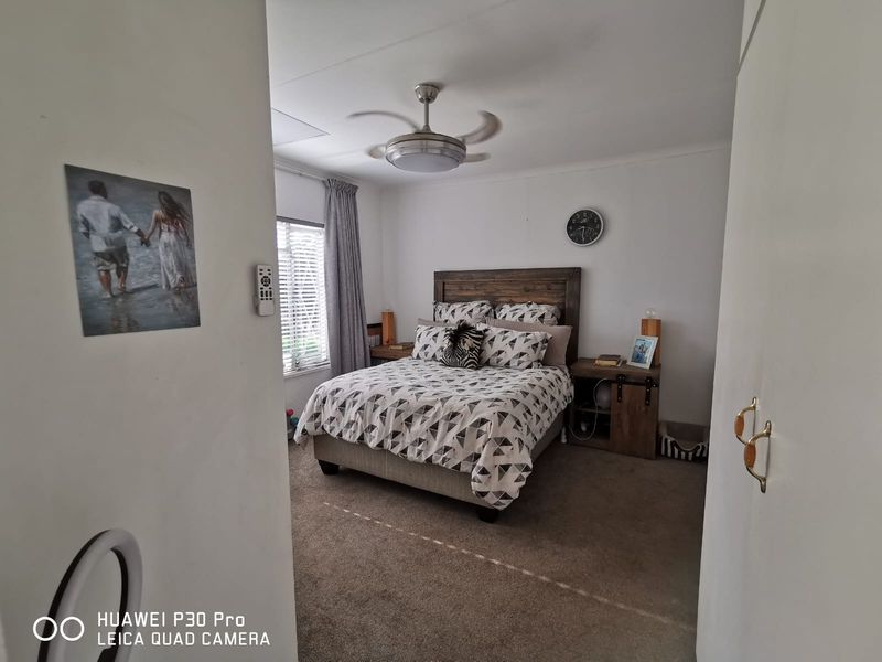 A carpeted bedroom featuring a ceiling fan and window blinds, offering a functional and comfortable sleeping space.