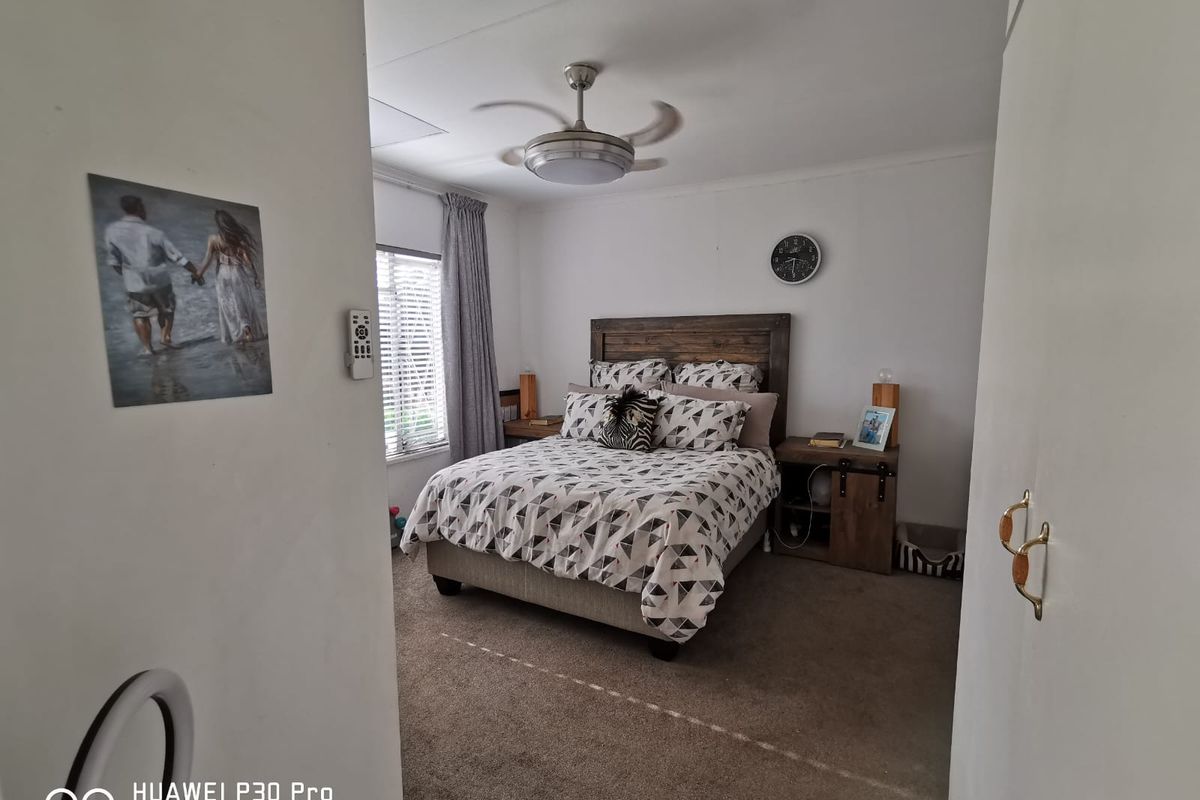 A carpeted bedroom featuring a ceiling fan and window blinds, offering a functional and comfortable sleeping space.