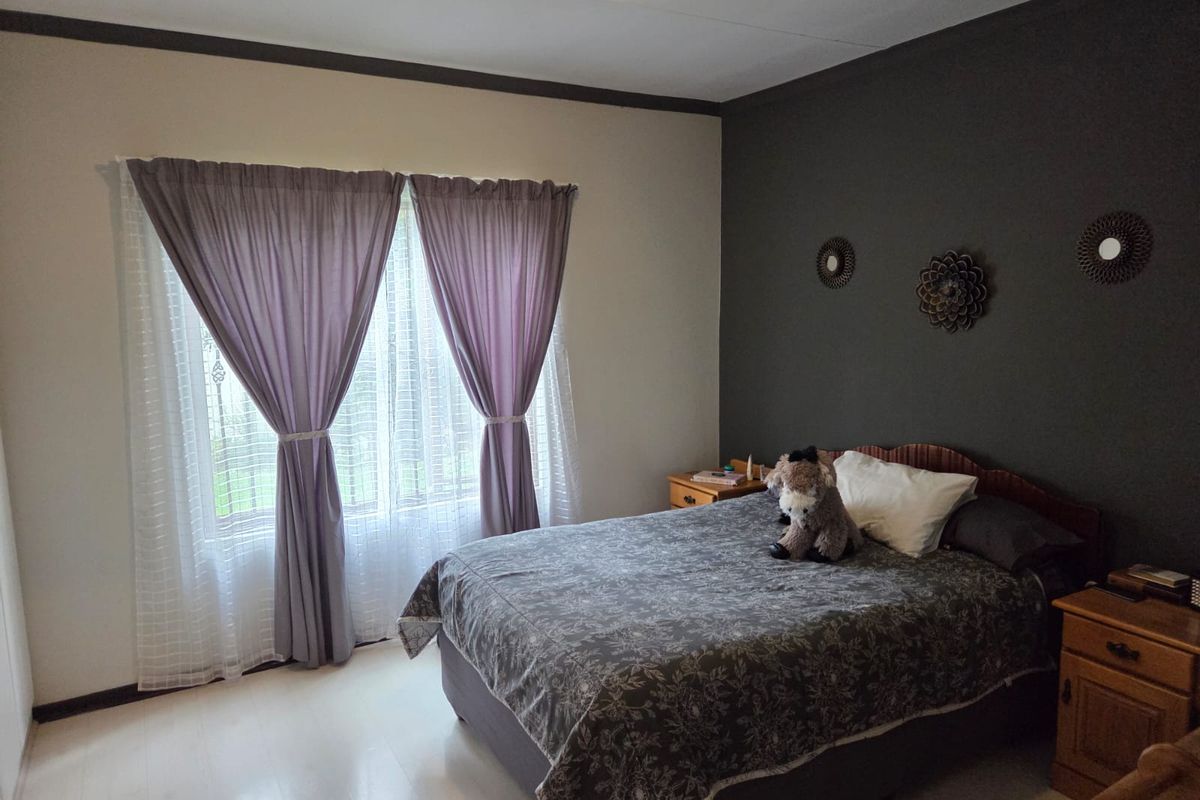 A well-lit bedroom featuring a dark accent wall, neutral flooring, and large windows with curtains.