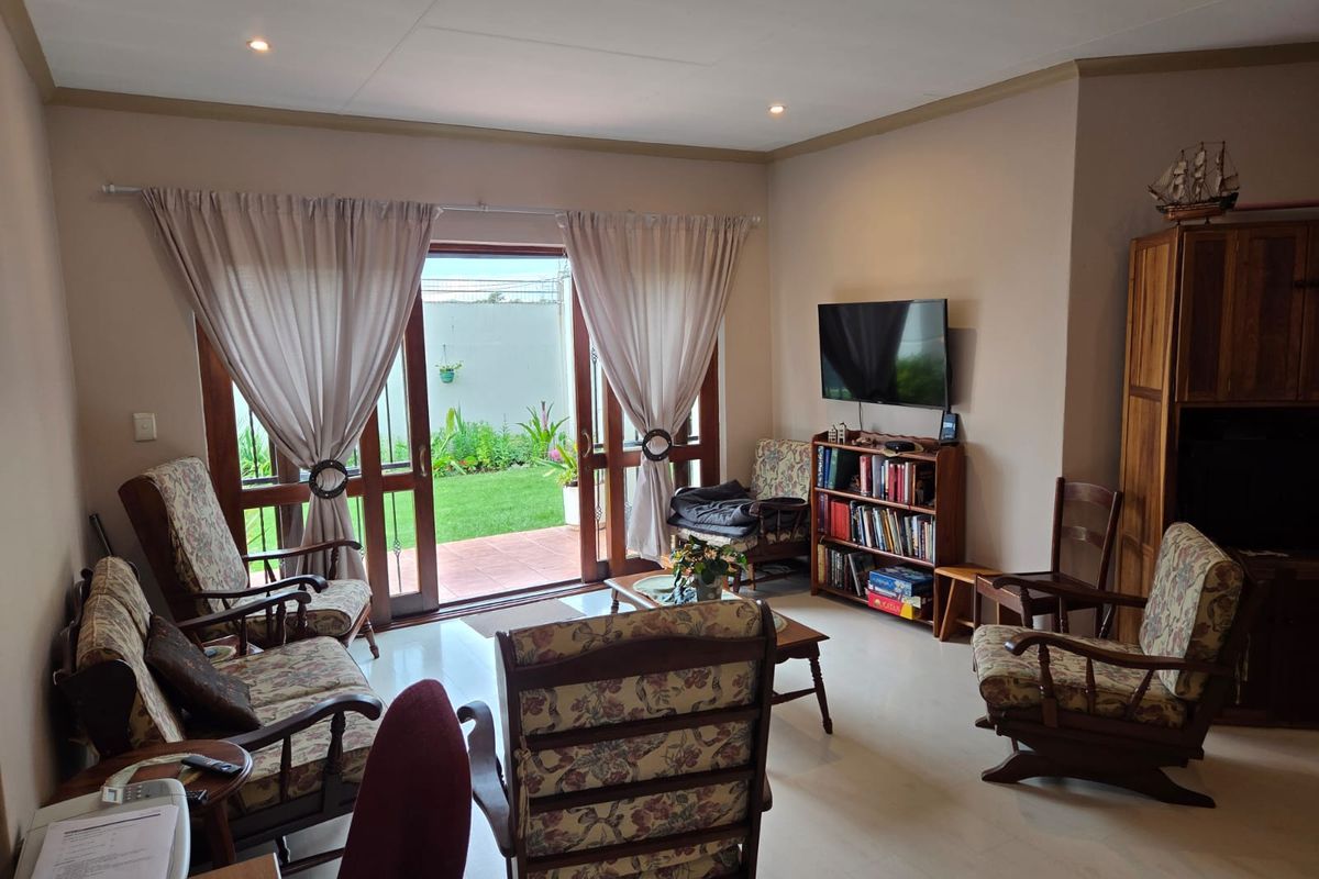 A comfortable living room featuring tiled flooring, recessed ceiling lighting, and large sliding glass doors that open onto a private rear patio and garden.
