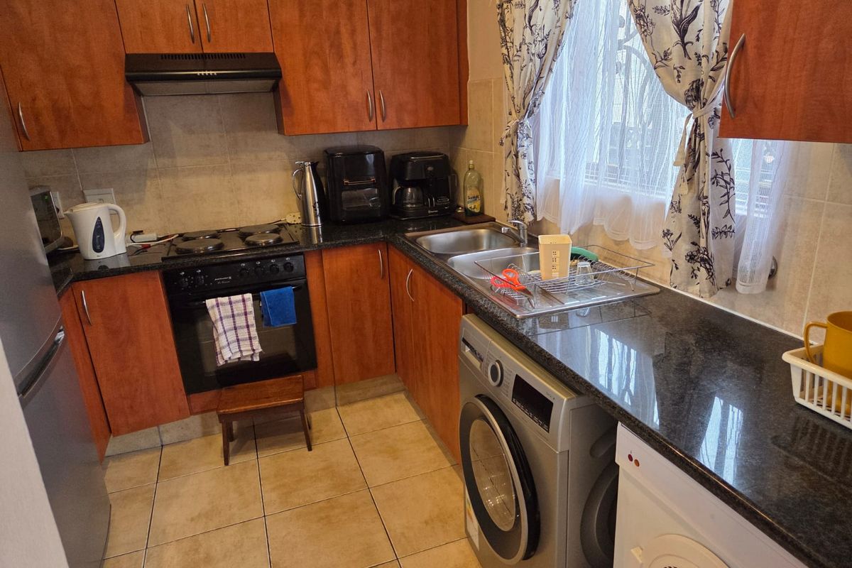 A functional kitchen featuring wood-finish cabinetry, granite countertops, a built-in oven with hob, extractor fan, and integrated plumbing for laundry appliances.