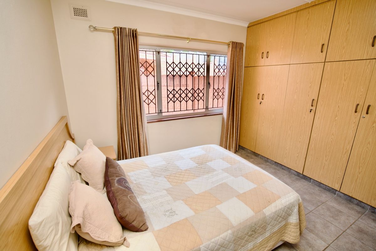 A bedroom featuring built-in wooden cupboards, tiled flooring, and a window fitted with a security gate.