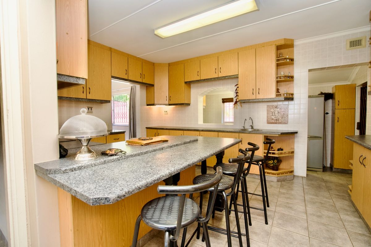 A functional kitchen featuring wood-look laminate cabinetry, granite countertops, a breakfast bar, and tiled flooring, offering a classic layout with ample storage space.