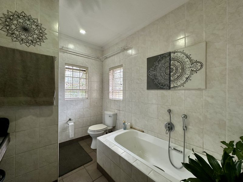 A functional bathroom featuring a built-in bathtub, toilet, and neutral wall tiling, offering a clean and practical space.