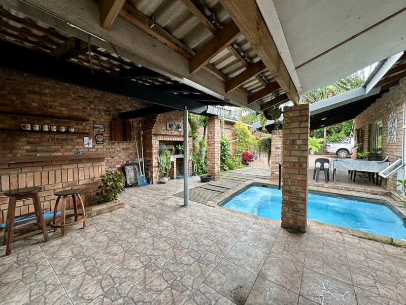 Covered outdoor entertainment area featuring a built-in brick braai, tiled flooring, and a swimming pool, ideal for relaxed social gatherings.