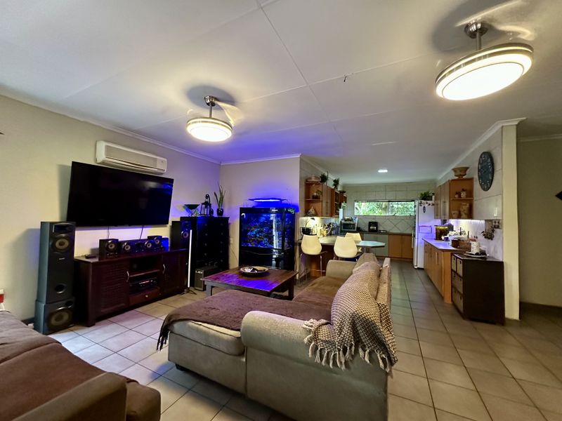 Spacious open-plan living and kitchen area featuring tiled flooring, split-system air conditioning, and functional built-in cabinetry with a breakfast bar.