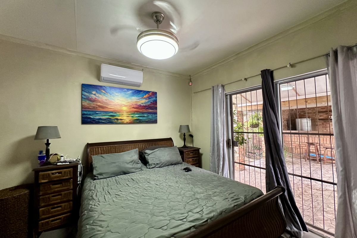 A bedroom featuring a ceiling fan, split-system air conditioning, and sliding glass doors with security gates providing access to an outdoor patio area.