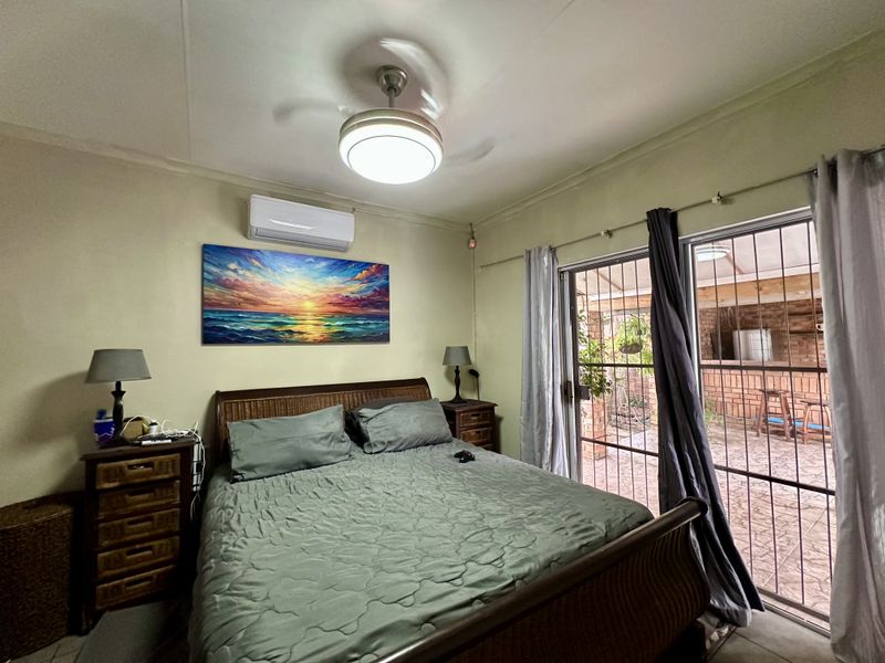A bedroom featuring a ceiling fan, split-system air conditioning, and sliding glass doors with security gates providing access to an outdoor patio area.