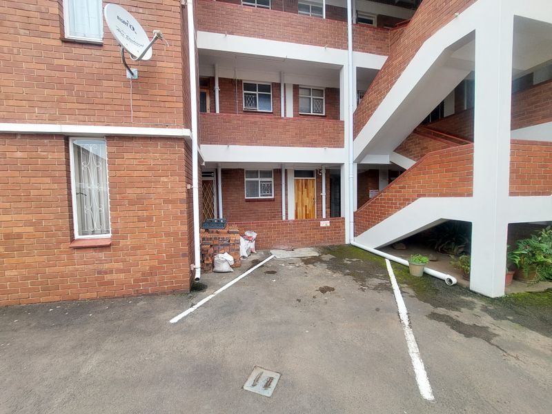 Exterior view of a brick apartment building featuring a concrete staircase, parking bay, and security-fitted windows.