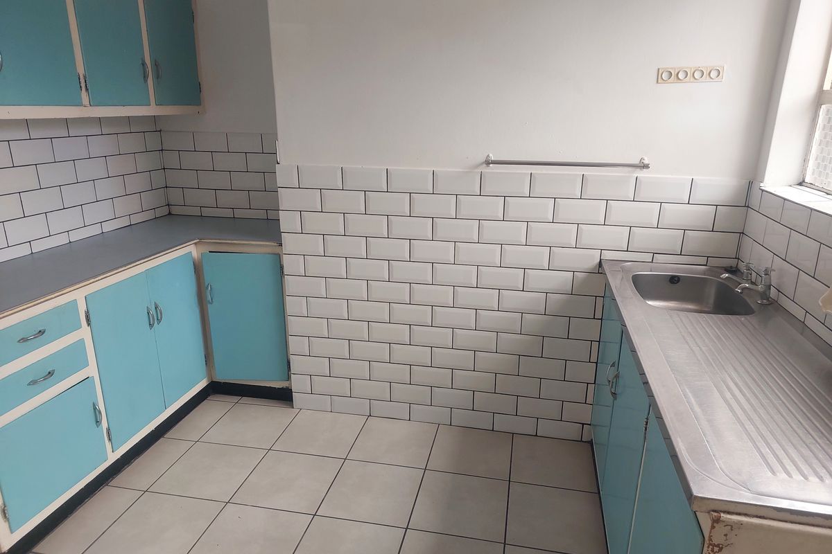 A functional kitchen space featuring subway tile backsplashes, stainless steel sink, and blue cabinetry, offering a blank canvas for modern renovation.