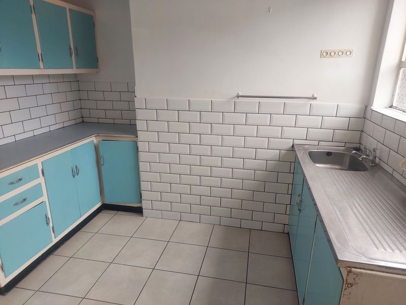 A functional kitchen space featuring subway tile backsplashes, stainless steel sink, and blue cabinetry, offering a blank canvas for modern renovation.